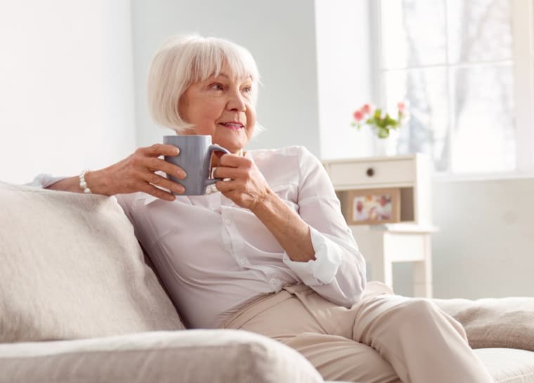 Amica Safety at Home Whitepaper Panel A senior woman enjoying a cup of coffee on her sofa at home